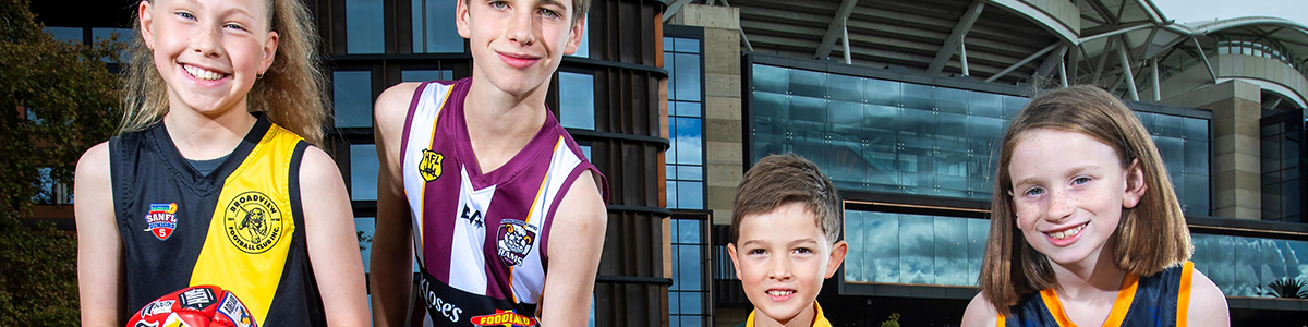 Four children in football guernseys standing in front of Adelaide Oval