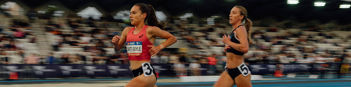 Two women running in front of a crowd on an athletics track