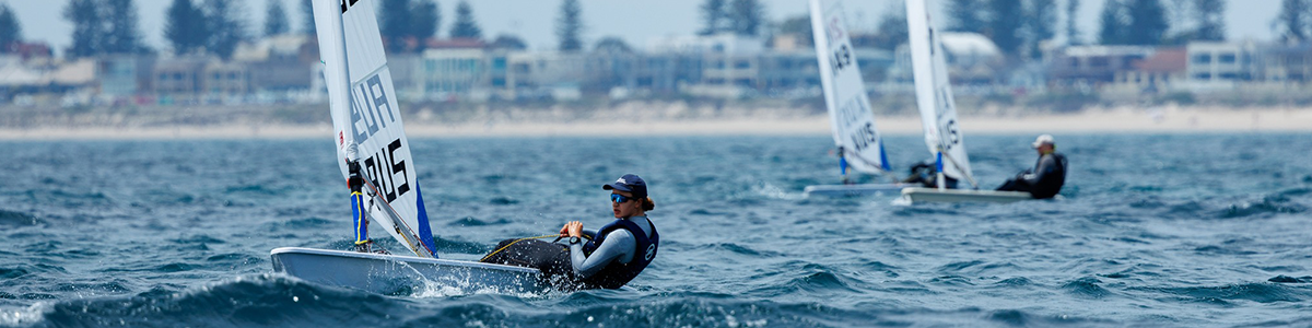 A woman in a sail boat on the water with boats in the background
