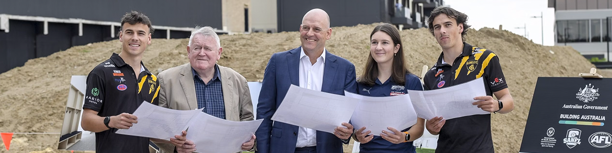 Footballers and executives hold up plans in front of a construction site